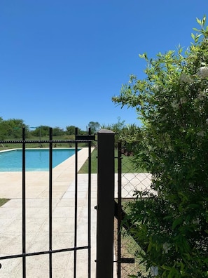 A gated pool area with a clear sky, surrounded by greenery. - Las Piedras Cabañas (General Belgrano)