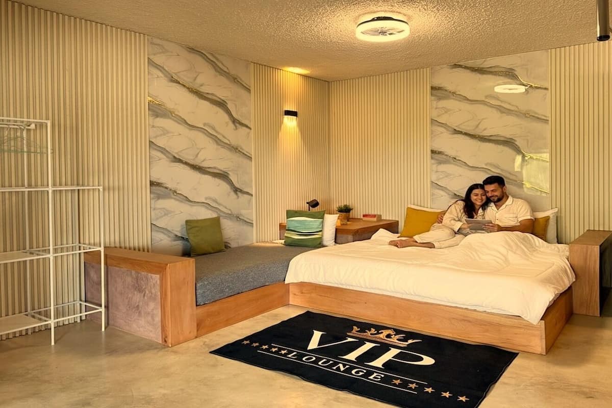 A hotel room with a bed, a bedside table, a nightstand, a small seating area, and a decorative rug.