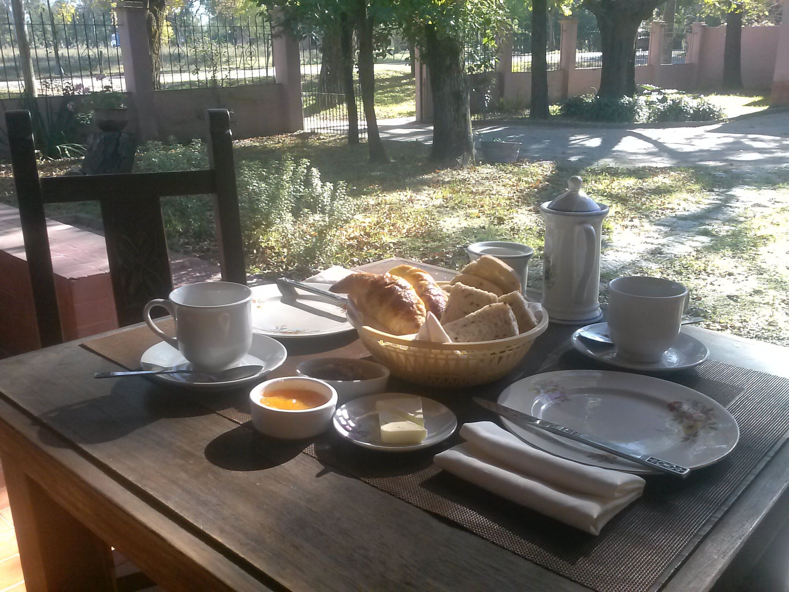 Una mesa de desayuno dispuesta con una taza, un tazón de sopa, un plato con mantequilla, una cesta de pan y una tetera.