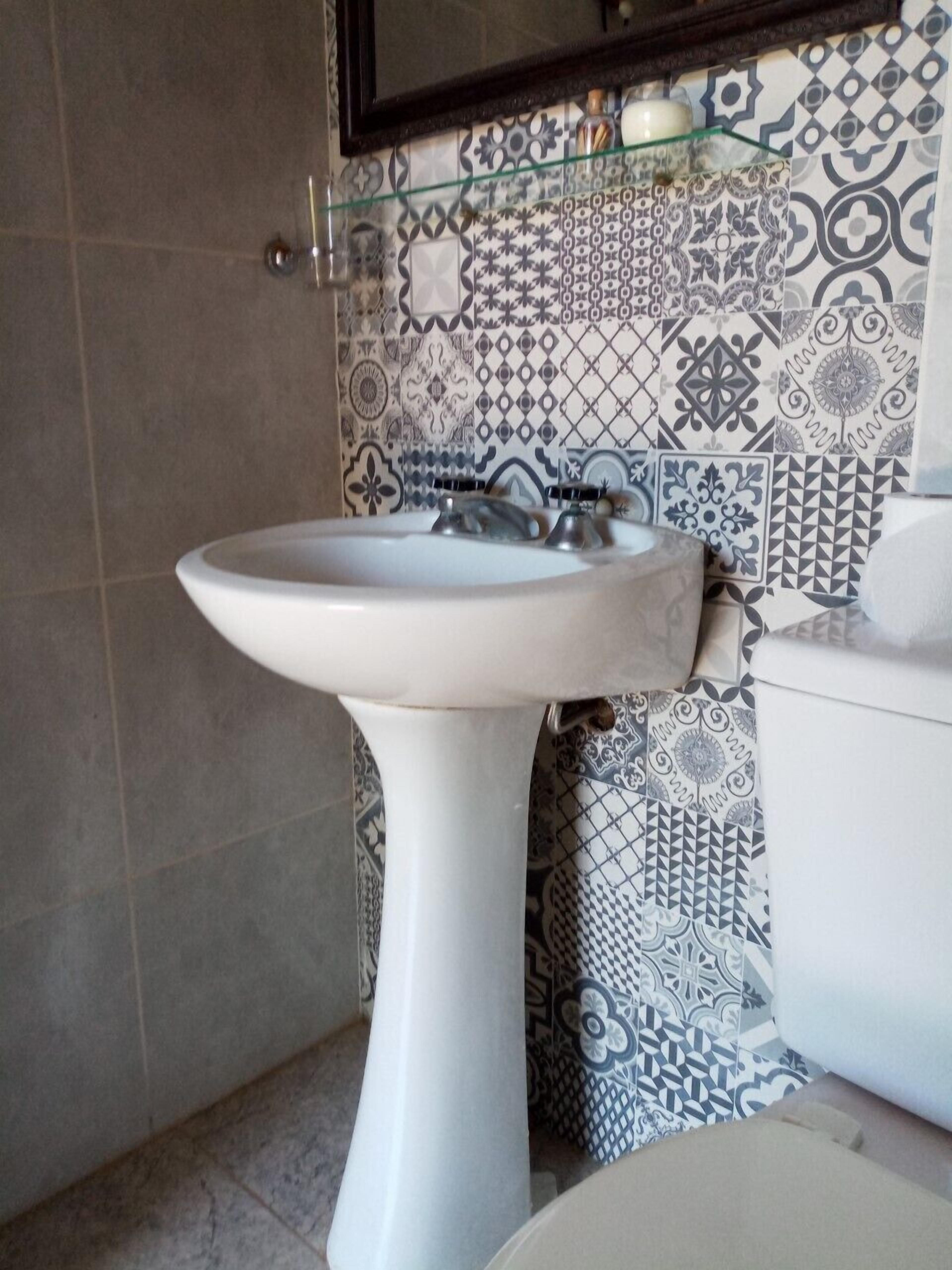 Une salle de bain avec un lavabo sur colonne blanc, des toilettes et des carreaux décoratifs sur les murs.