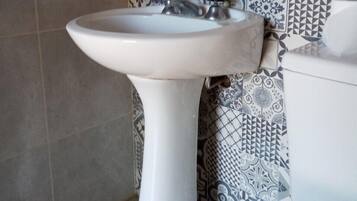 Une salle de bain avec un lavabo sur colonne blanc, des toilettes et des carreaux décoratifs sur les murs.