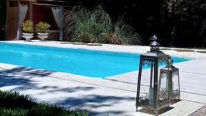 En swimmingpool med en dekorativ lykta, omgiven av krukväxter och träd.