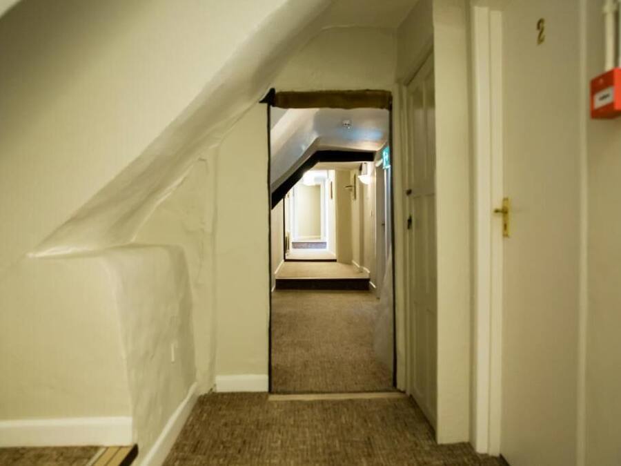 A narrow hallway with a carpeted floor, a door on the right, and a visible staircase leading to an upper level.