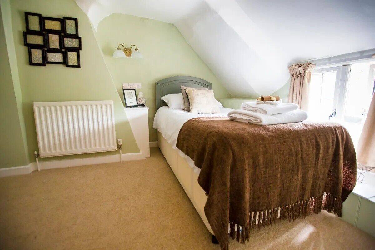 A bedroom with a bed, a radiator, a window with curtains, and wall-mounted picture frames.