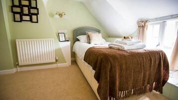 A bedroom with a bed, a radiator, a window with curtains, and wall-mounted picture frames.