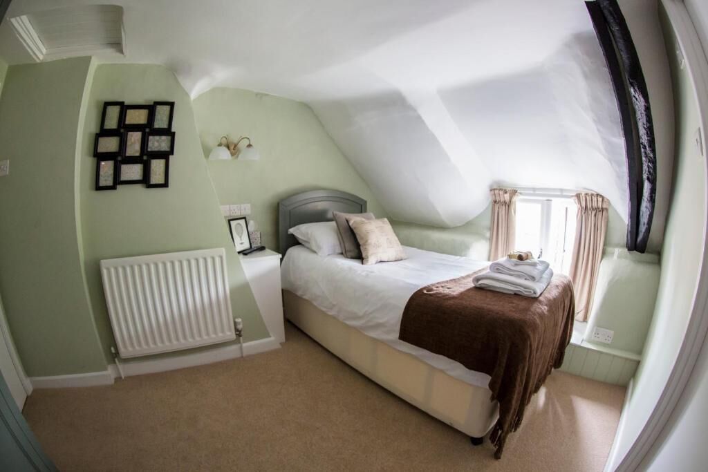 A bedroom with a bed, a radiator, a wall-mounted picture frame, and a window with curtains.