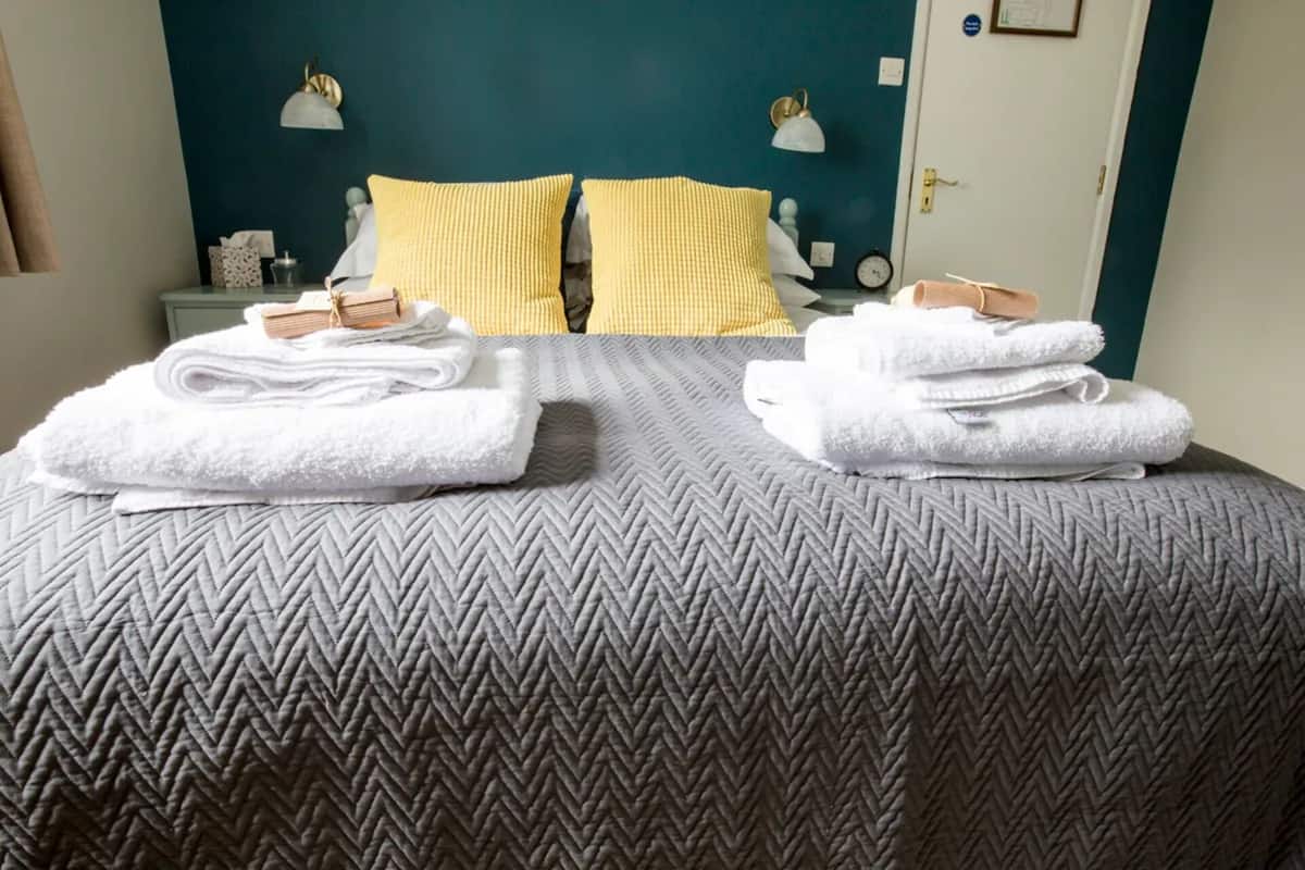 A hotel room with a bed, two pillows, a nightstand, and two towels.