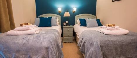 Une chambre double avec deux lits, chacun équipé d’un oreiller et d’une serviette, une table de chevet avec une lampe et une horloge murale.