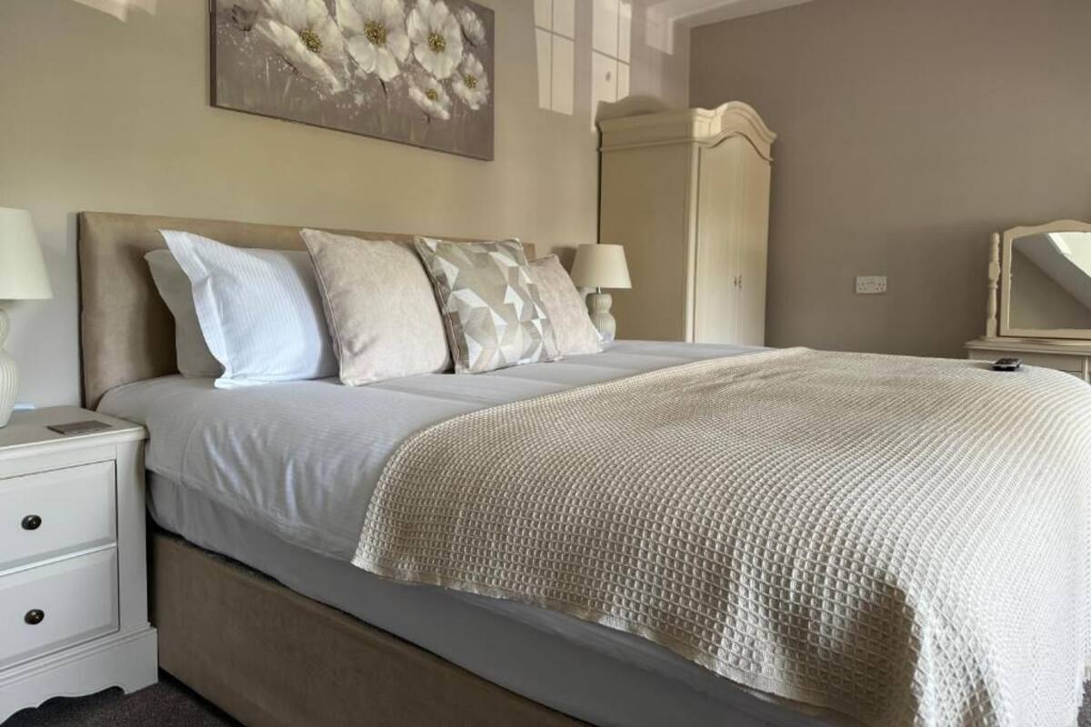 A bedroom with a bed, nightstands, a dresser, a mirror, and a floral painting on the wall.
