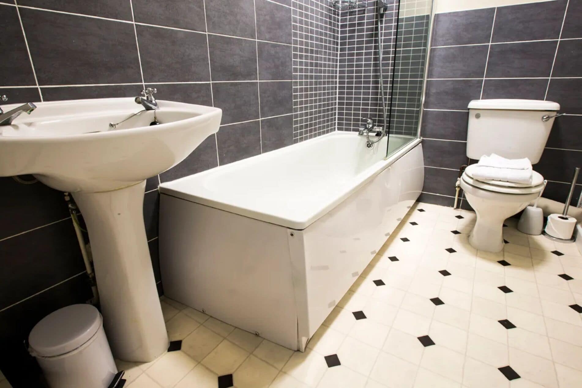 A bathroom with a bathtub, sink, toilet, and a trash bin.