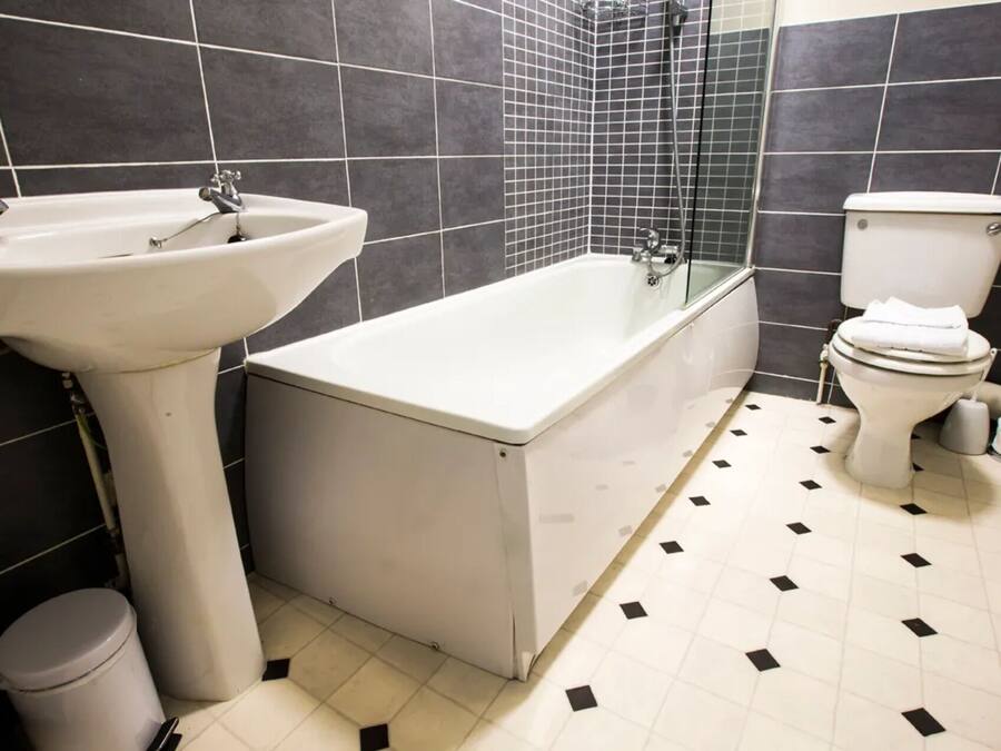 A bathroom with a bathtub, sink, toilet, and a trash bin.