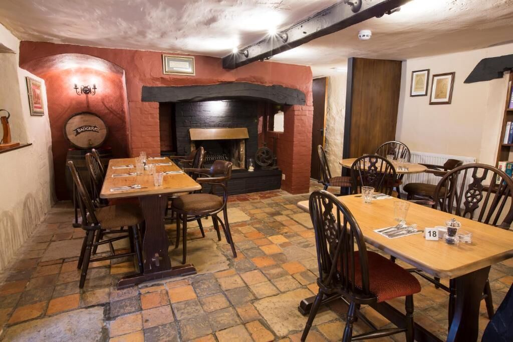 Un pub tradicional con mesas y sillas de madera, una chimenea de ladrillo y un suelo de piedra.