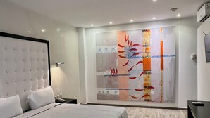 Une chambre moderne avec un grand lit, une table de chevet, un téléviseur fixé au mur et une œuvre d’art abstraite originale accrochée au mur.