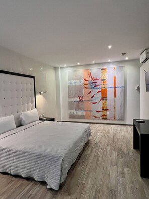 Quarto moderno com uma cama grande, mesa de cabeceira, TV na parede e uma obra de arte abstrata na parede.