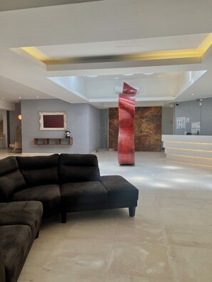 A modern reception area with a reception desk, a large red sculpture, a black leather sofa, and a marble wall. - Rubra Hotel & Spa (Playa del Carmen)
