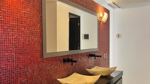 Une salle de bain avec un mur recouvert de mosaïques rouges, un grand miroir et deux vasques en bois.