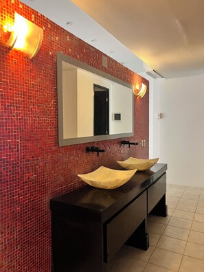 Casa de banho com parede em mosaico vermelho, um espelho grande e duas pias de madeira.