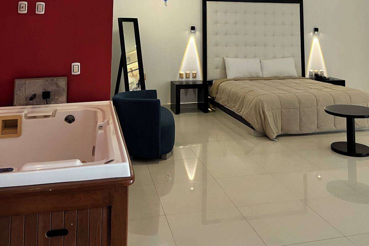 Une chambre à coucher moderne avec un grand lit, des lampes de chevet, une petite table et une baignoire.