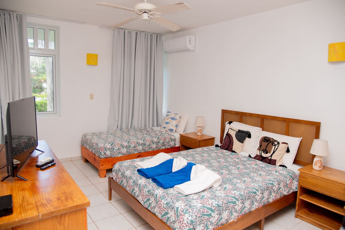 A hotel room with two beds, a TV, a ceiling fan, and a window with curtains.