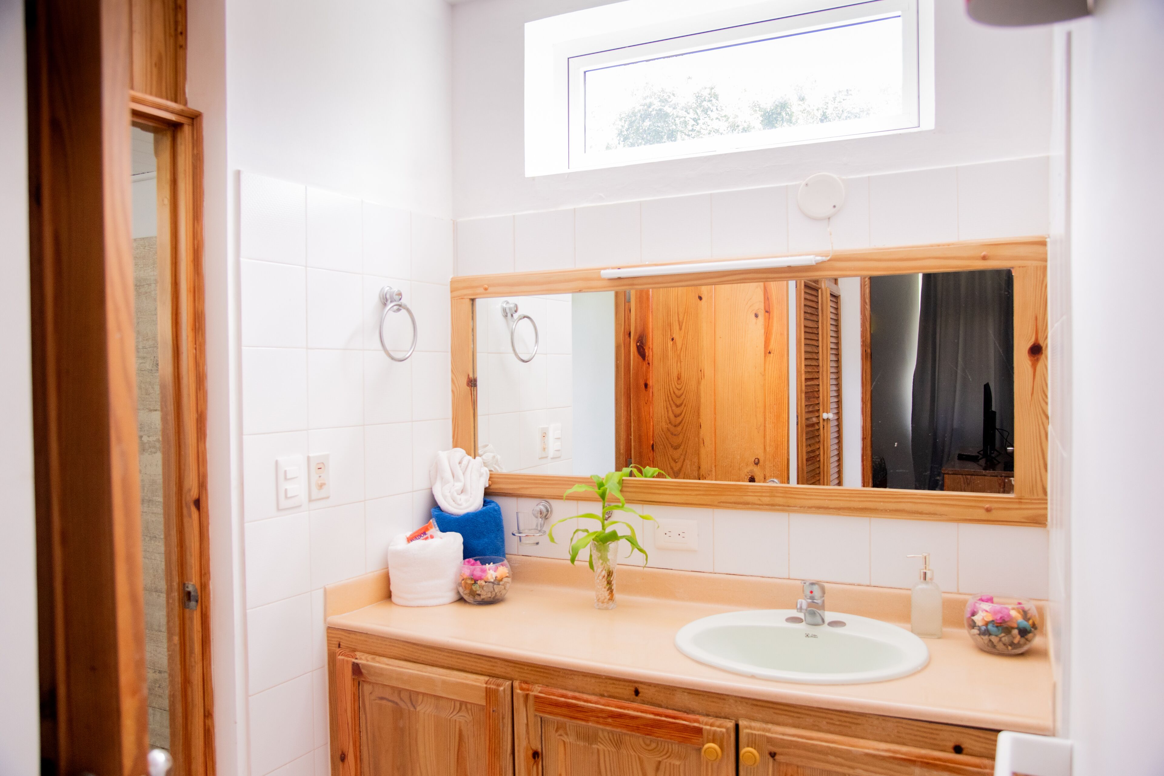 A bathroom with a wooden vanity, a white sink, a mirror, and a window above the mirror.