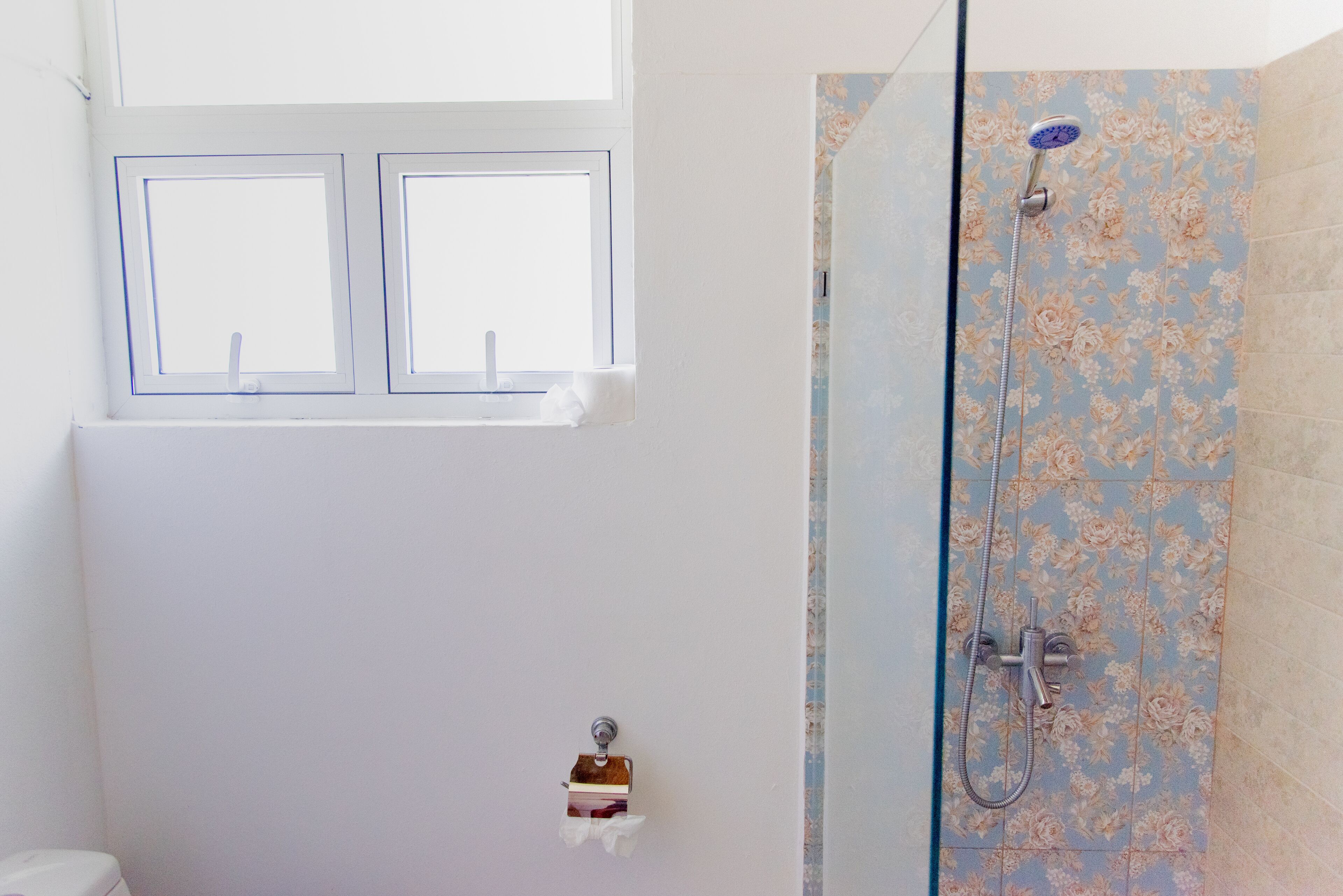 Et badeværelse med brusebad, toilet og et vindue.