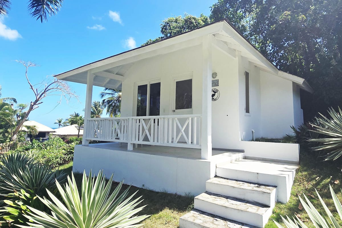A white building with a covered porch, steps leading up to the entrance, and a small sign on the wall.