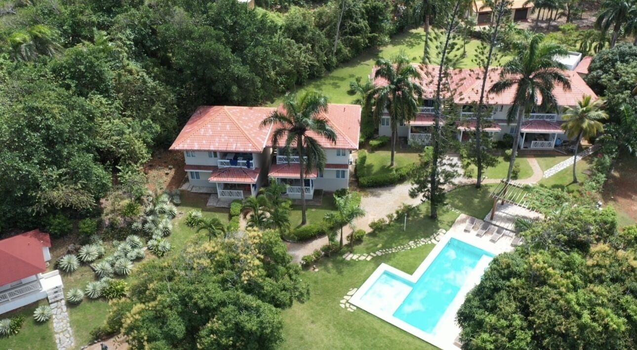 A large building with multiple balconies, surrounded by lush greenery and a swimming pool.