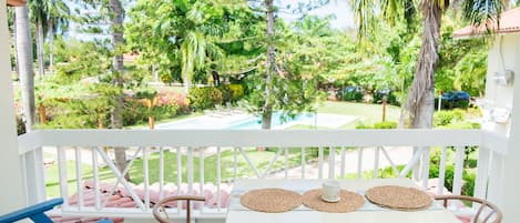 A covered outdoor seating area with a table and chairs, overlooking a garden with a pool.