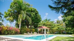 Une piscine entourée de chaises longues, d’un belvédère et d’une végétation luxuriante.