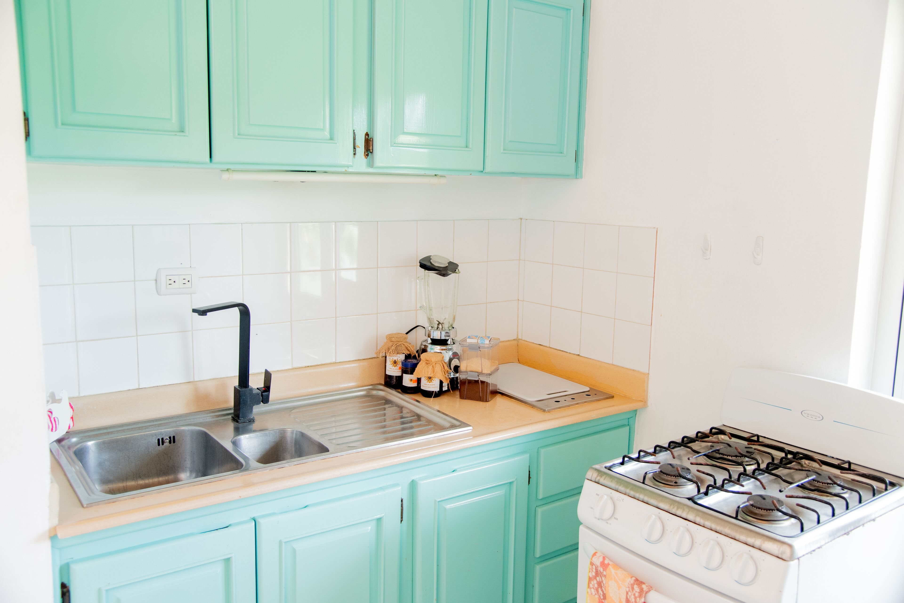A kitchen with teal cabinets, a double sink, a stove, and a countertop with various items.