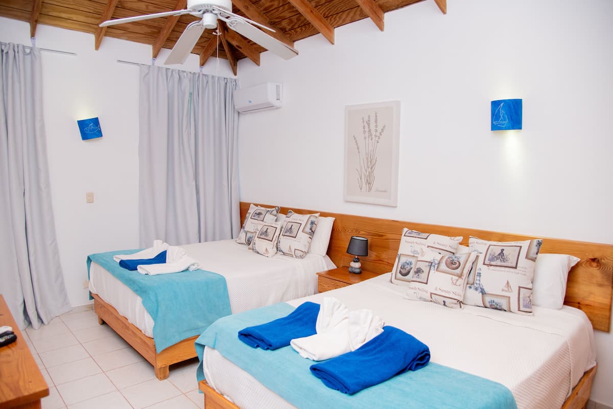 A hotel room with two beds, a ceiling fan, an air conditioner, and a framed picture on the wall.