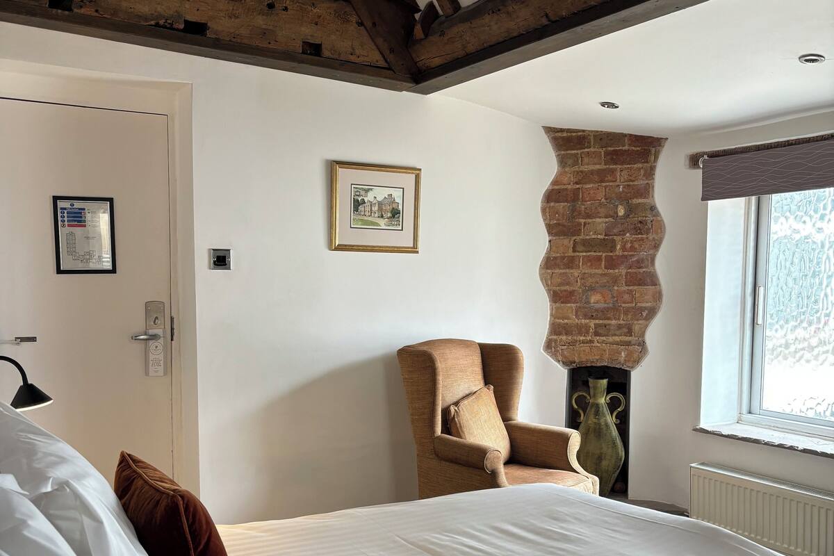 A bedroom with a large bed, a chair, a fireplace, and a window.