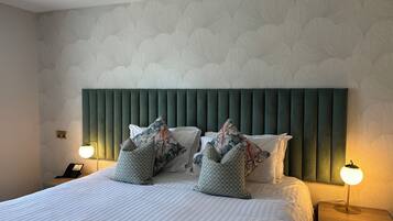 A neatly made bed with striped bedding, a green upholstered headboard, and decorative pillows. There are bedside lamps on either side of the bed, and a phone on the nightstand.