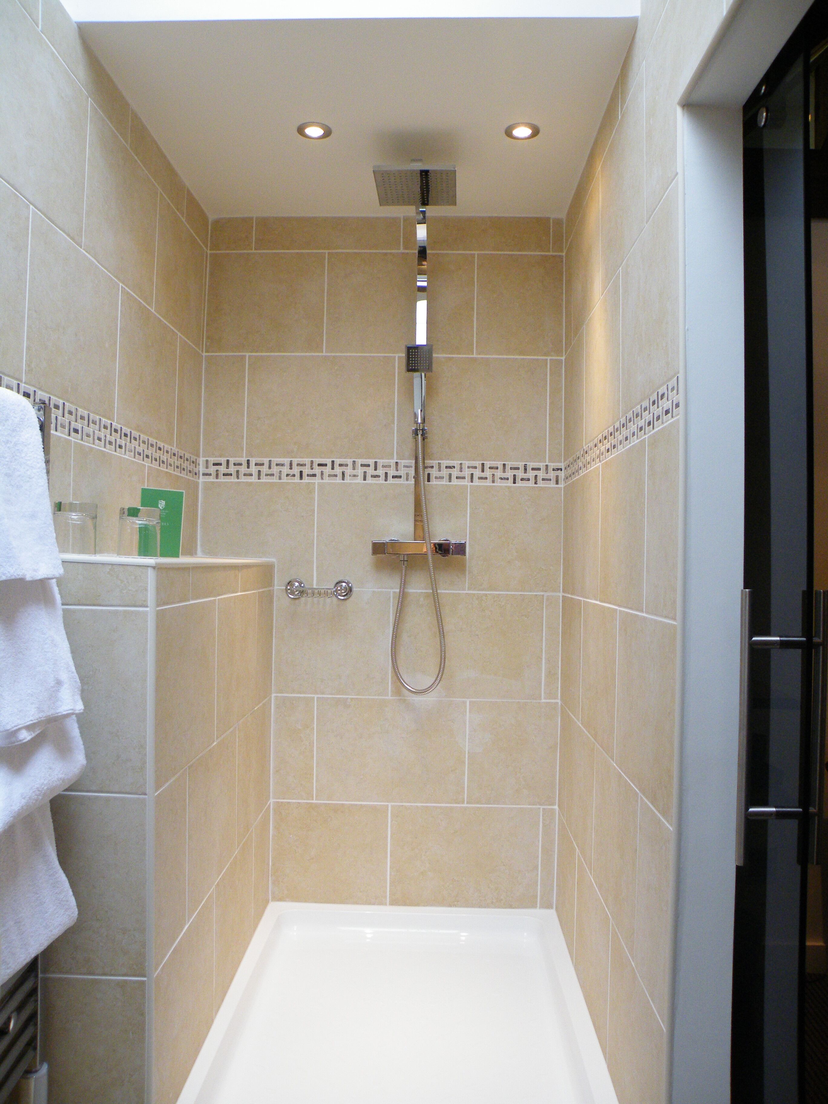 A small, tiled shower room with a handheld showerhead and a wall-mounted faucet.