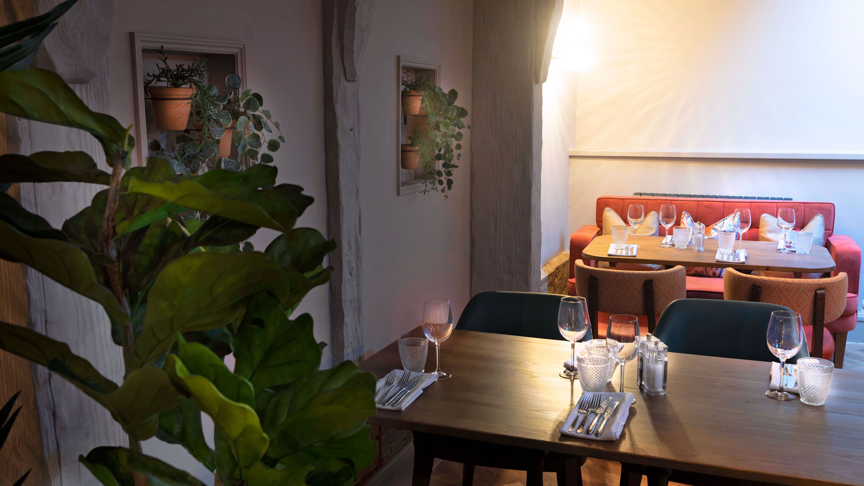 A dining area with a wooden table set for two, two chairs, and a red cushioned bench in the background.