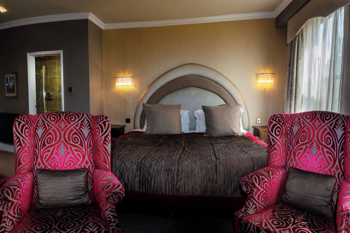 A hotel room with a large bed, two armchairs, a nightstand, and a mirror.