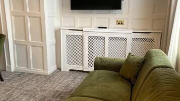 A living room with a green sofa, a flat-screen TV mounted on a white wall, and a white entertainment unit below it.