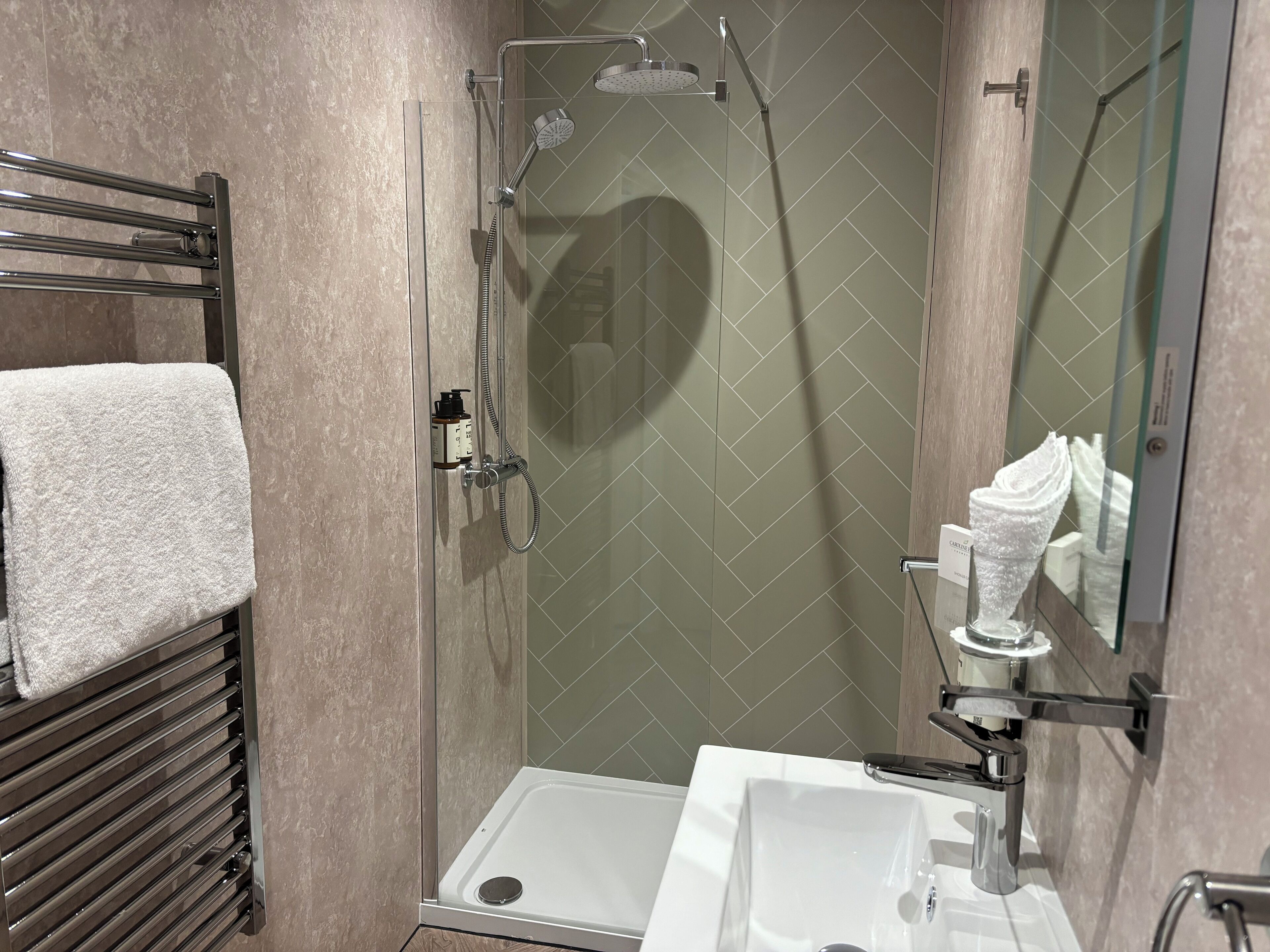 A modern bathroom with a glass-enclosed shower, a white sink, and a towel rack.