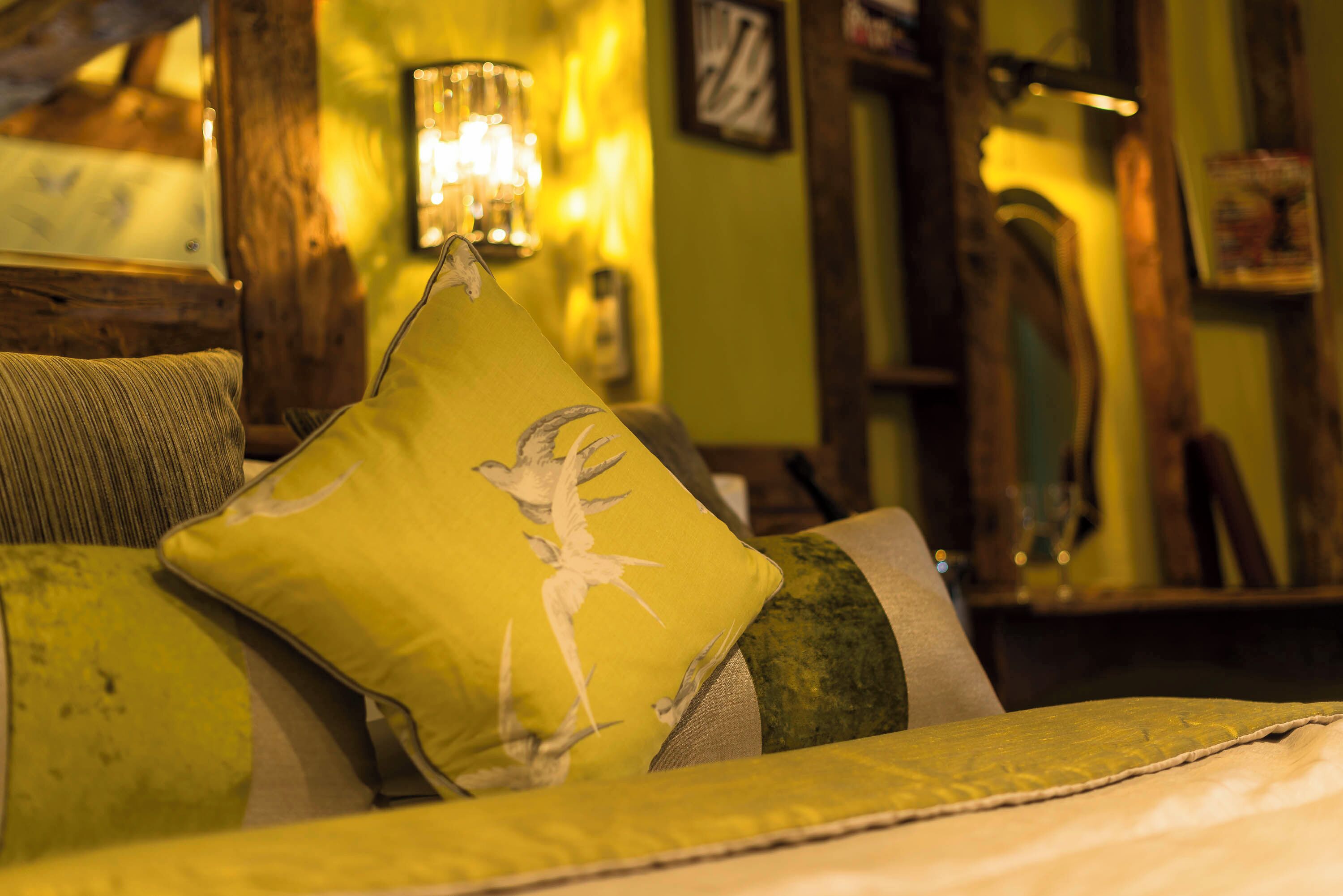 Una habitación acogedora con una cama, un almohadón verde con diseño de pájaro y una lámpara.