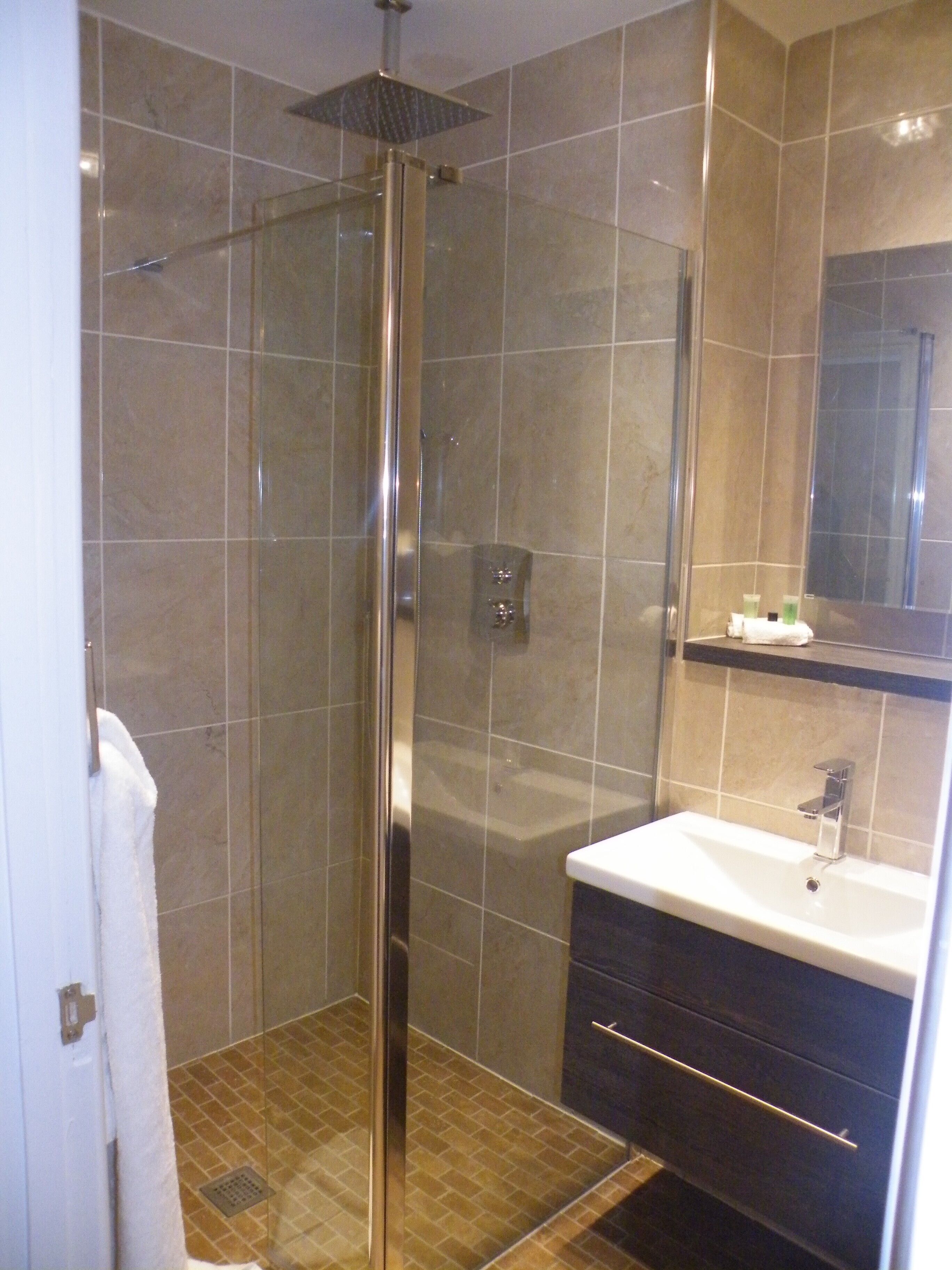 A modern bathroom with a glass-enclosed shower, a sink with a mirror above it, and a towel hanging on the wall.