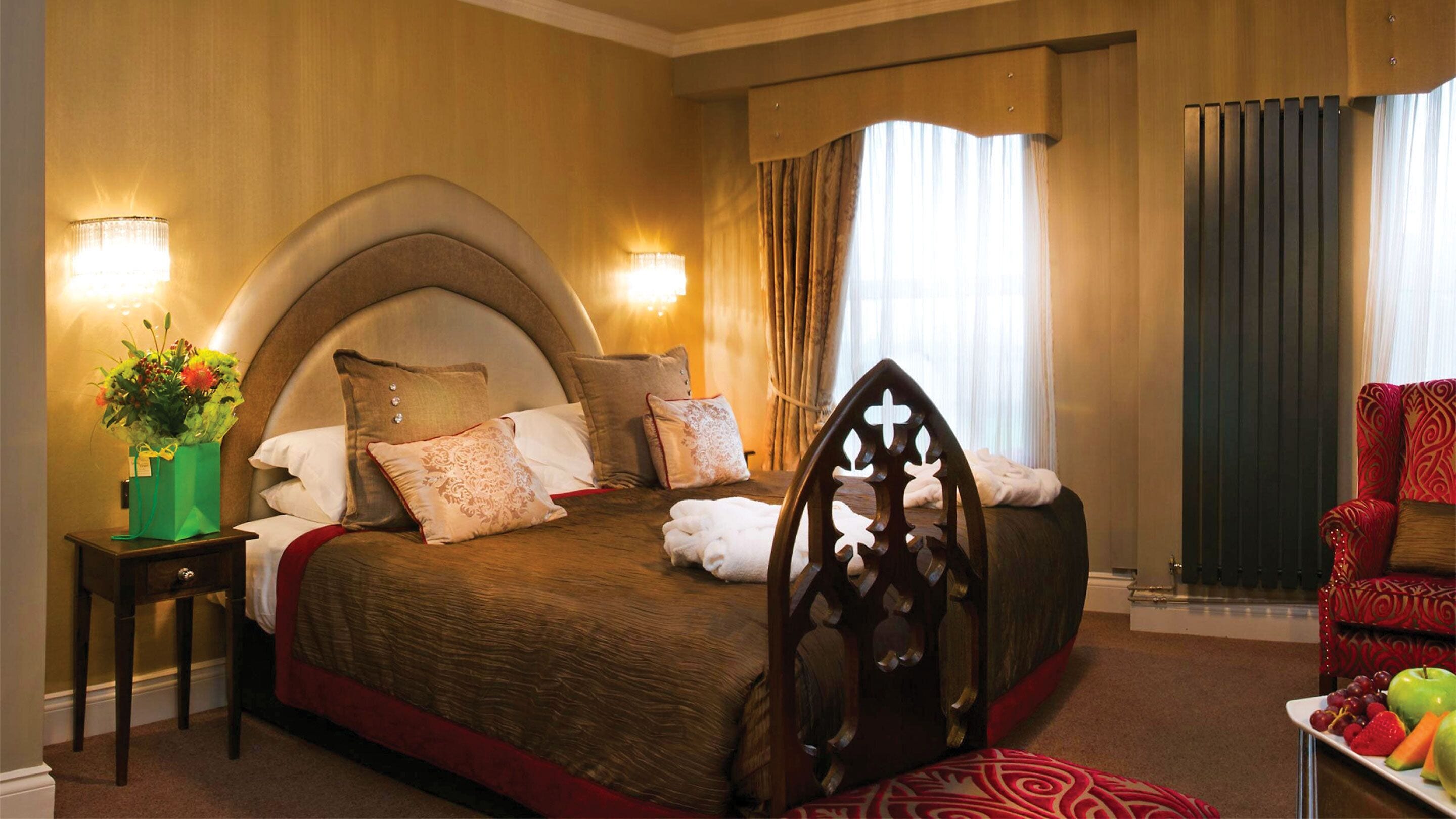A hotel room with a large bed, a wooden chair, a nightstand with a vase of flowers, and a fruit plate on the side table.