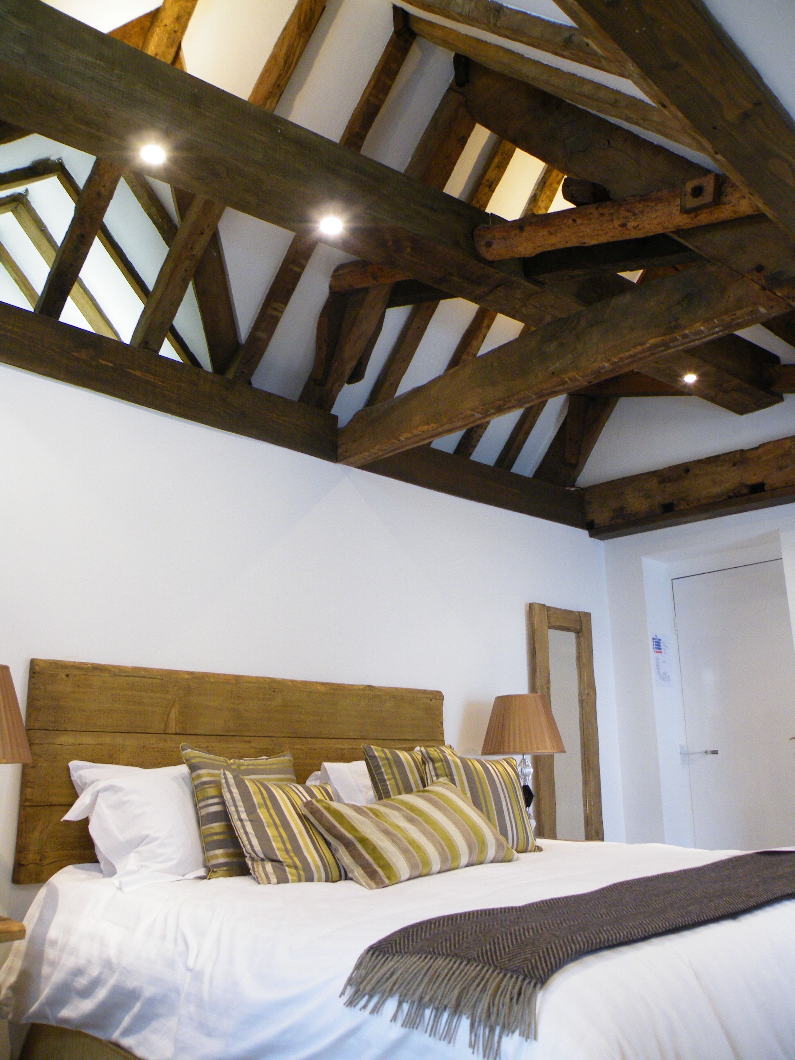 A bedroom with a wooden ceiling, a bed with white bedding and striped pillows, and two bedside lamps.