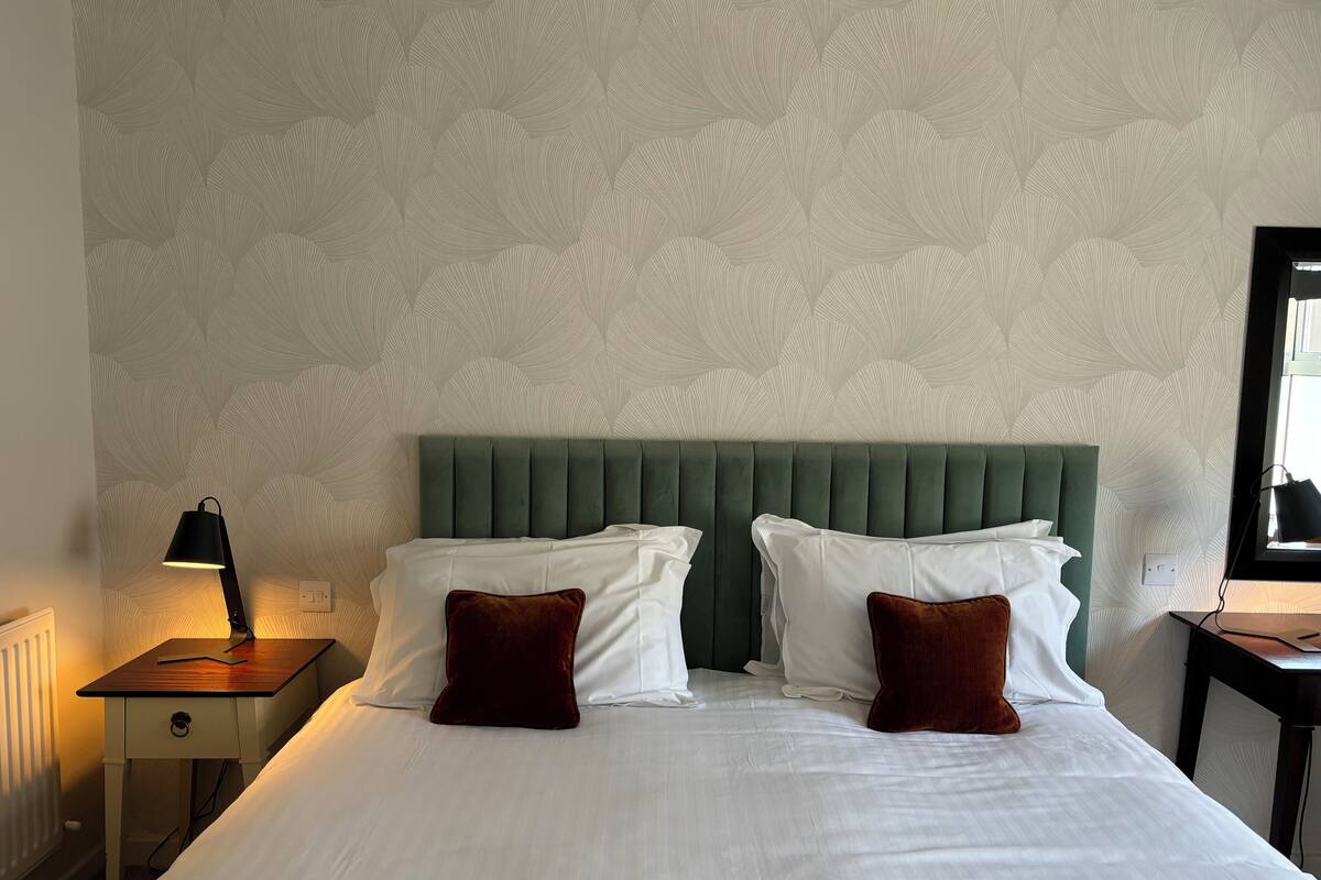 A hotel room with a green upholstered headboard, white bedding, and two brown pillows.
