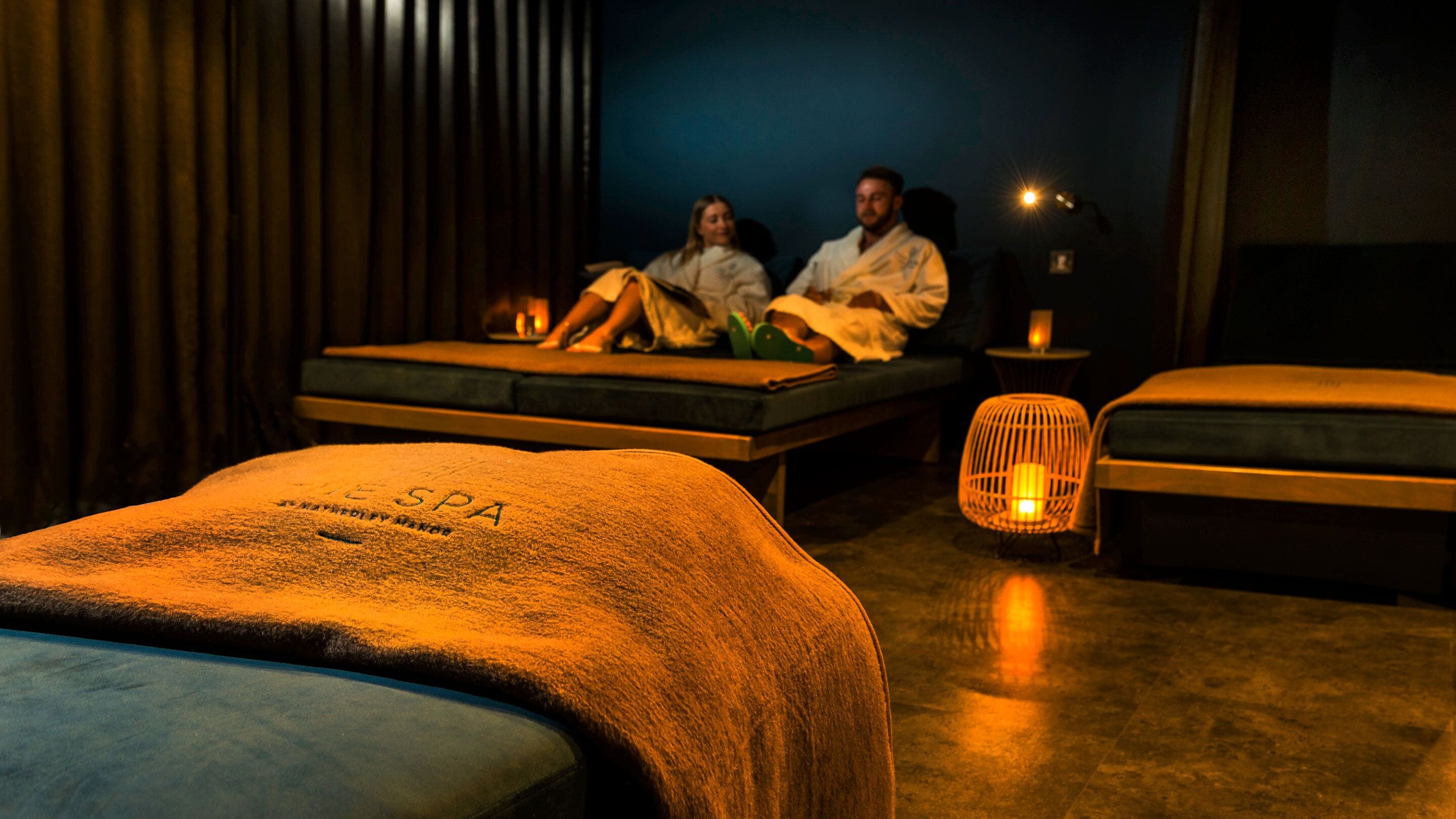 Un cuarto de spa con dos camillas de masaje, una mesita con lámpara y un calentador fijado a la pared.