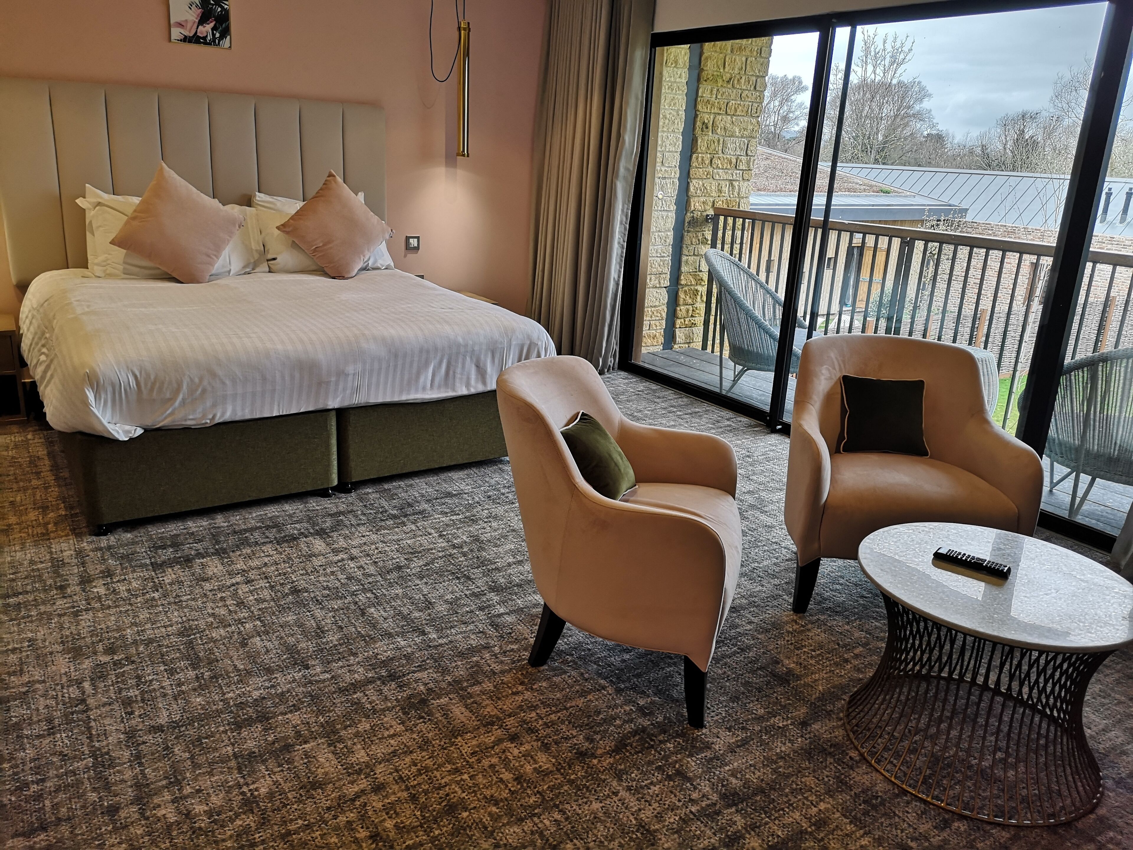 A hotel room with a large bed, two armchairs, a small table, and a balcony with a view.