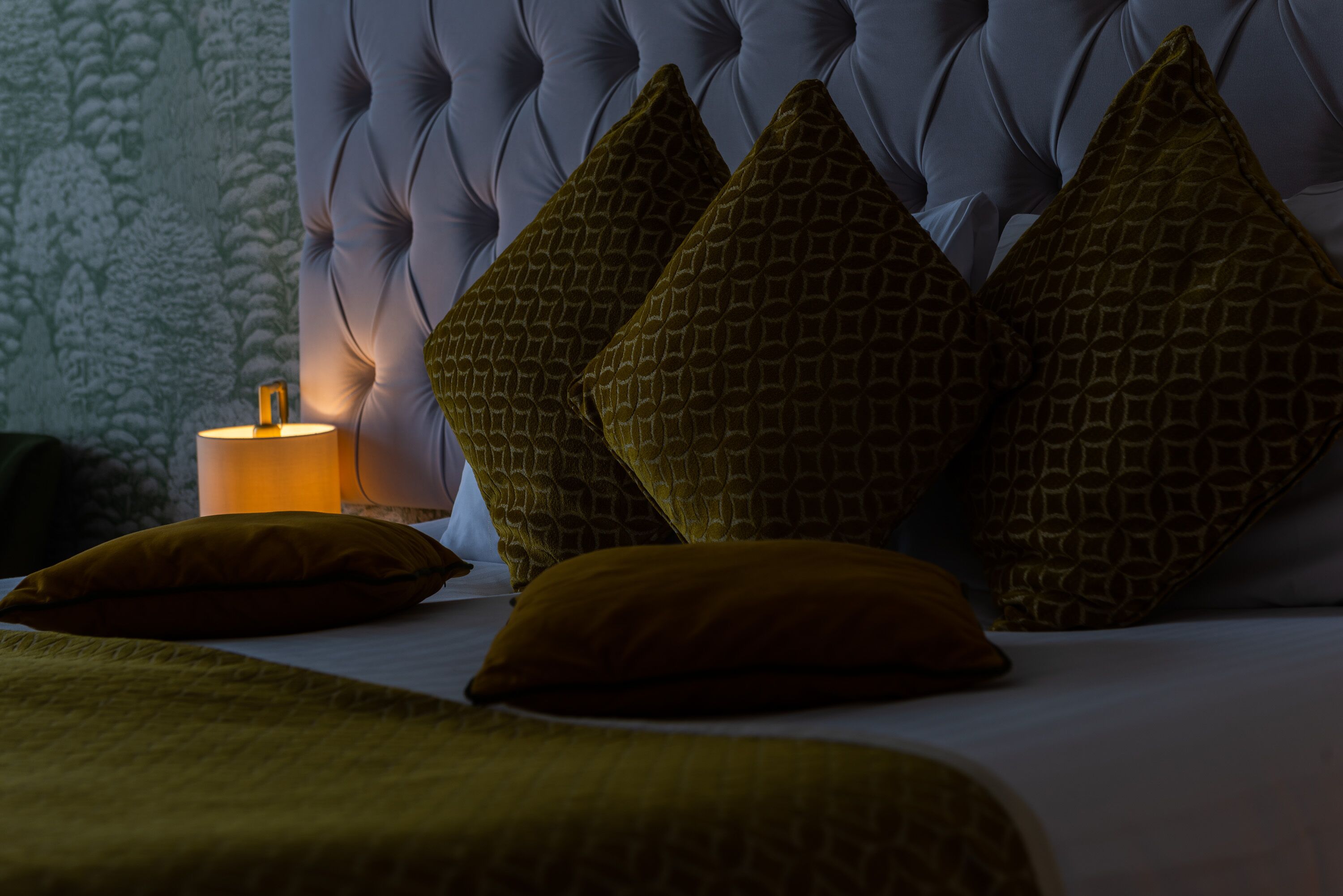 A bed with a tufted headboard, multiple pillows, and a bedside lamp.