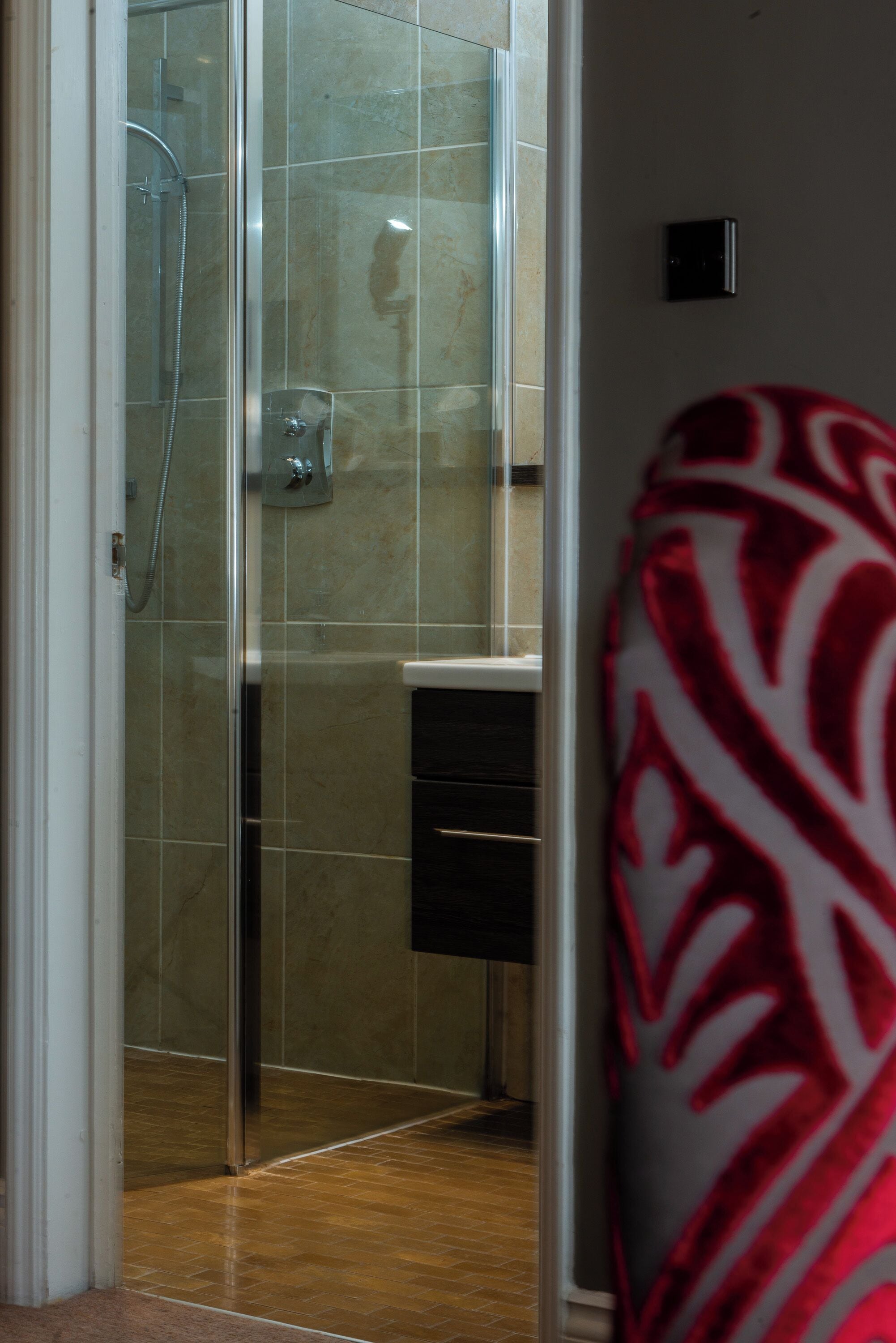 Un baño con cabina de ducha de vidrio, lavamanos y toalla estampada.