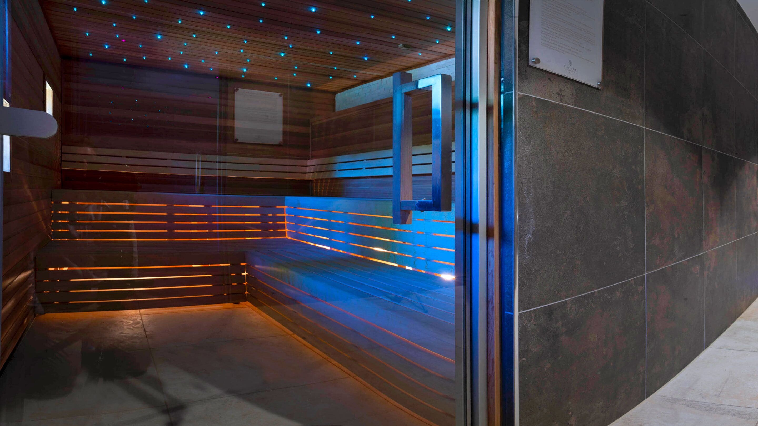 A modern spa room with a wooden ceiling, a glass partition, and a bench.