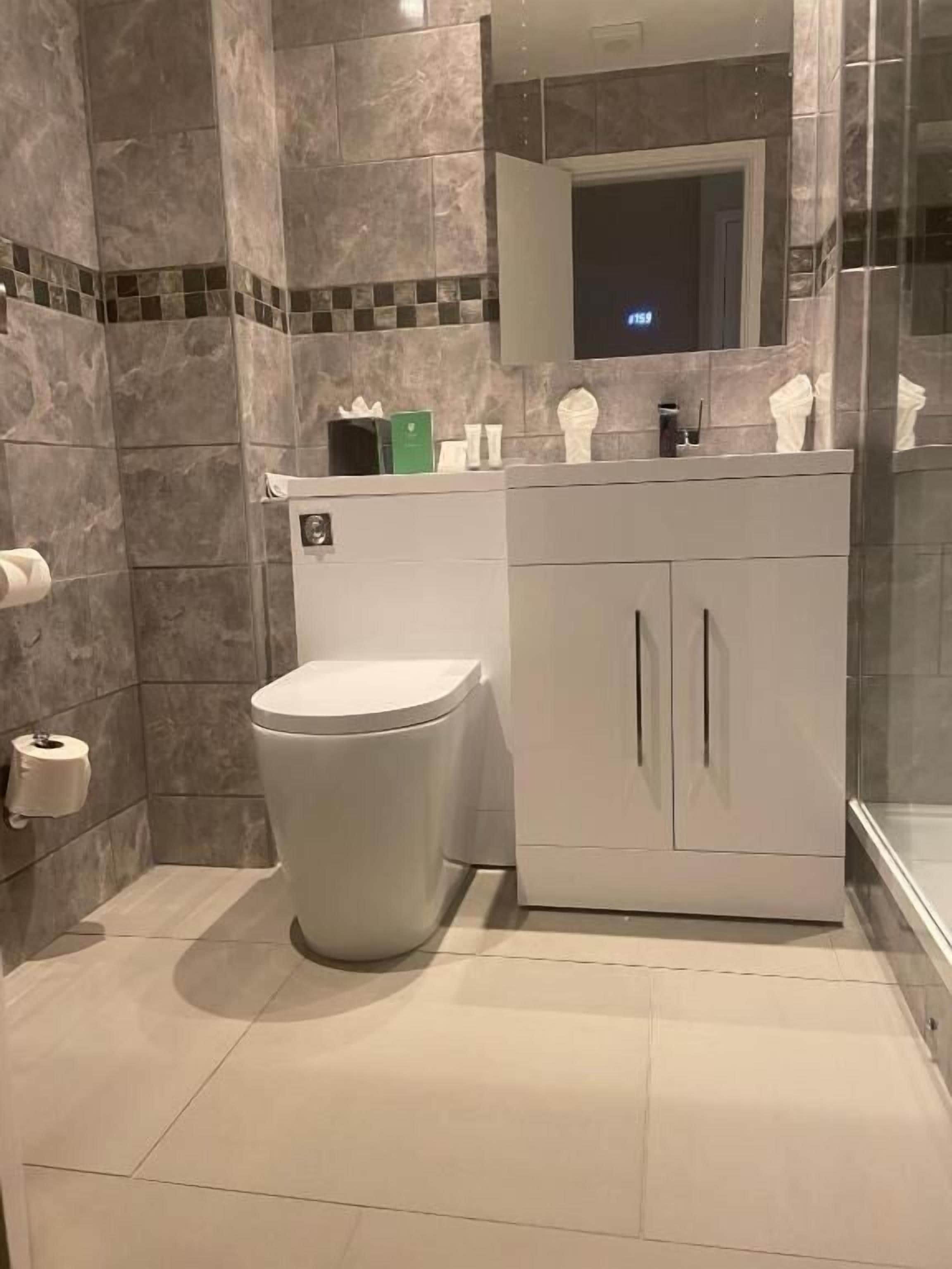 Ein modernes Badezimmer mit Toilette, Waschbecken mit Spiegel und Pflegeprodukten auf der Ablagefläche.