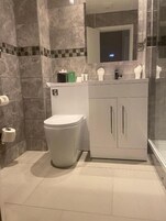 Un baño moderno con inodoro, lavabo con espejo y artículos de aseo en la encimera.